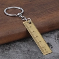 Mini vintage brass ruler keychain measuring tool with 6cm scale on rustic wood background - Antique Bronze