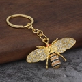 Gouden bijen sleutelhanger met kristallen en emaille op een houten ondergrond - Goud