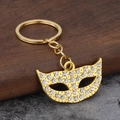 Sparkling gold masquerade mask keychain with clear rhinestones on a rustic wood surface - Gold