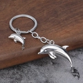 Detail van een zilveren 3D-dolfijn sleutelhanger met kleine hanger op een oppervlak - Wit K/Zilver