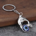 Detail eines silbernen Delfin-Schlüsselanhängers mit blauer Evil Eye Perle auf Holz - Delfin