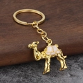 Nahaufnahme eines goldenen Kamel-Schlüsselanhängers mit rosa Emaille-Details - Gold Weiß