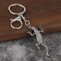 Silberner Gecko-Schlüsselanhänger mit Strasssteinen auf Holz- und Steinhintergrund - Gunmetal