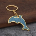 Portachiavi a forma di delfino blu glitterato con catena dorata su sfondo di legno e pietra - Oro