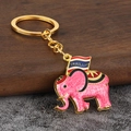 Macro detail of a pink Thai elephant keychain with a Thailand flag on a wooden block - Pink