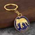 Detalle de un llavero de recuerdo de Tailandia con elefante dorado sobre esmalte azul - Morado