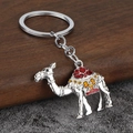 Macro view of silver camel keychain with red and yellow enamel saddle on desert sand background - Silver & Red
