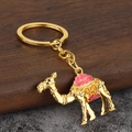 Détail d'un porte-clés chameau doré avec émail rose et rouge sur un sol en marbre - Or + Rose