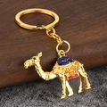 Détail d'un porte-clés chameau doré avec motifs en émail sur surface en bois sombre - Or + Bleu