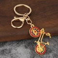 Detail of golden bicycle keychain with red rhinestones and lobster clasp on wood background - Gold Red Stone