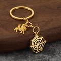 Golden spider and web keychain charms displayed on a rustic wood block background - Gold