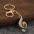 Llavero dorado de clave de sol con pedrería brillante sobre fondo de textura natural - Oro + Diamantes de Imitación Blancos
