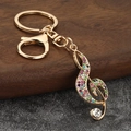 Detalle de un llavero de nota musical con diamantes de imitación sobre superficie de piedra - Oro + Diamantes de Imitación Multicolor