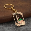 Detailed close-up of golden Madina mosque keychain with pink flowers and engraving - Pink