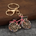 Detailed view of pink bicycle keychain with colorful rhinestones on a dark wood block - Gold + Pink