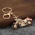 Detailed close-up of golden motorcycle keychain with sparkling rhinestones and pink enamel - Gold + Pink