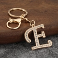 Close-up of gold letter E keychain with pavé rhinestones on walnut and stone background - Letter E