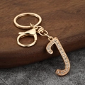 Detailed view of a gold-tone letter J keychain with clear rhinestones on a wooden stand - Letter J
