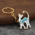 Eleganter Emaille-Katzen-Schlüsselanhänger in Goldoptik mit Blumenmuster auf Holzhintergrund - Gold Weiß
