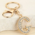 Detail of gold letter G keychain with sparkling white rhinestones on stone background - Letter G