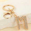 Macro detail of golden letter M keychain with crystal rhinestones on stone background - Letter M