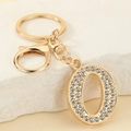 Detail of gold letter O keychain with white rhinestones and lobster clasp on stone surface - Letter O