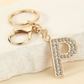 Close-up of gold metal letter P keychain with sparkling rhinestones on stone background - Letter P