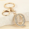 Close-up of gold-plated letter Q keychain with sparkling crystals on white marble - Letter Q