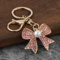 Close-up of pink rhinestone bow keychain with white pearl on golden metal base - Pink