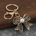 Detail of a gold-plated bow keychain with black rhinestones and a white imitation pearl - Black