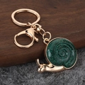 Detail of a snail-shaped gold keychain with sparkling green resin shell on wood surface - Gold-Green