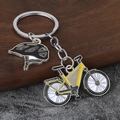 Detail of metal keychain featuring yellow mountain bike and black cycling helmet charms - Yellow