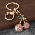Gouden kersensleutelhanger met roze strass-steentjes en blad op houten achtergrond - Roze