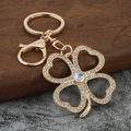 Golden four-leaf clover keychain with rhinestones and iridescent crystal on wood background - White Zirconia