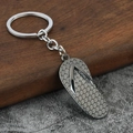 Detail of flip-flop shaped metal keychain with textured sole on a rustic wood background - Gunmetal