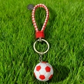 Dettaglio portachiavi calcio bianco e rosso con cinturino intrecciato su prato verde - Calcio Rosso con Cordino Intrecciato