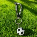 Detail of soccer ball keychain with black and white woven strap on green grass - Classic Football with Braided Strap