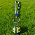 Close-up of yellow and blue volleyball keychain with braided leather strap on green grass - Classic Volleyball Style + Strap