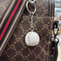 Detailweergave van een mini-honkbal sleutelhanger met rood stiksel aan een bruine rugzak - 2.7cm / Wit