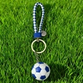 Blue and white checkered soccer ball keychain with woven strap on grass background - Blue Football with Braided Strap