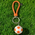 Orange and white football keychain with woven leather strap on green grass background - Orange Football with Braided Strap