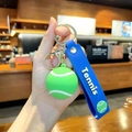 Tennis ball keychain with green silicone charm, blue wrist strap and gold metal hardware - Tennis
