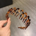 Tortoiseshell wavy headband with grip teeth for non-slip styling and hair volume - Amber / [product Attributes] This Product Is A Serrated Headband Visually Made Of Plastic Or Resin Featuring A Classic Tortoiseshell Texture (interwoven From Dark Brown And Amber). The Design Incorporates A Dense Comb-like Structure To Effectively Secure Stray Hairs And Add Volume To The Hairstyle. [visual Presentation] The Image Is A Real-life Photo Showing The Headband's Curvature Through A Hand-held Display Against A Gray Tiled Background. Image Quality Is [medium] With Good Clarity But The Lighting Is Slightly Direct. Aesthetics Are [medium] Overall Score [6.5]. While The Handheld Shot Showcases The Product The Background Appears Cheap And Lacks Brand Appeal. [text Content] There Is No Post-processing Or Background Text In The Image. [logistics Labels] None. [infringement Risk] Product Infringement: None As It Is A Generic Style. Background Infringement: None. [product Parameters] Tortoiseshell Color Serrated Structure Plastic Material.