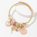 Pulsera dorada con dijes de océano, corazón de perla y concha sobre soporte blanco - Rosa