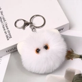 Close-up of a white fluffy monster keychain with big orange eyes on a book - Upgrade - Silver Ring / 8cm White