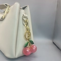Pink glittery cherry bag charm with green leaves and gold ring on a beige purse - Gold Green Leaf Double Pink Cherry