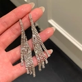 Gros plan de boucles d'oreilles à pompons en strass étincelants tenues à la main - Style à franges longues / Argent