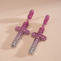 Un gros plan détaillé de boucles d'oreilles croix avec des strass dégradés roses - Rose