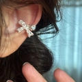 Vue rapprochée d'un élégant clip d'oreille en forme de nœud argenté orné de zircons. - Oreille gauche / Argent