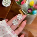Detail of silver camellia flower stud earrings with sparkling crystals held by a hand. - Camellia Style / Silver